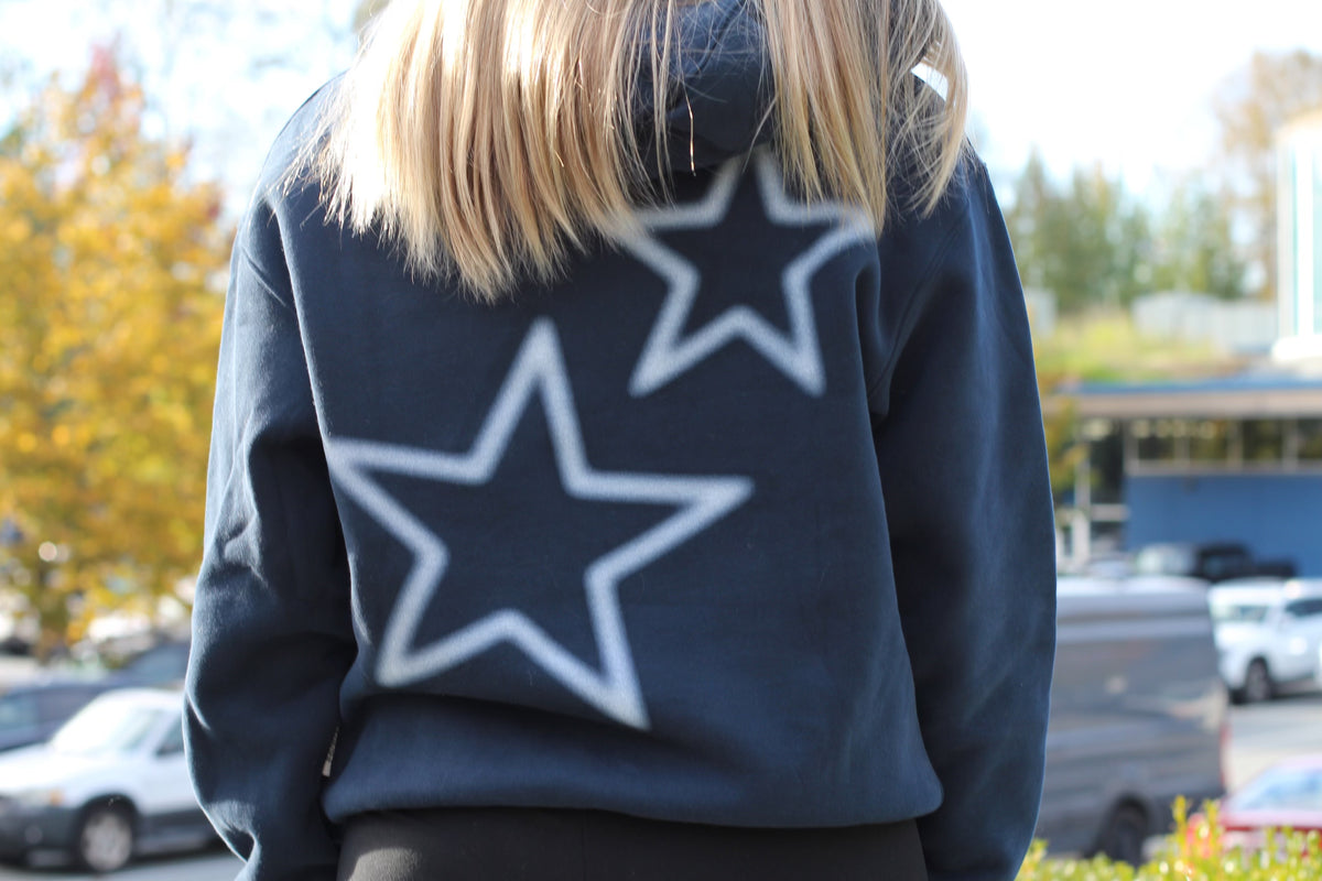 Person wearing a dark blue sweatshirt with a large white star on the back, standing outdoors.