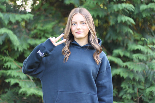 Person wearing a navy hoodie with 'Purelight' branding, making a peace sign in front of green trees.