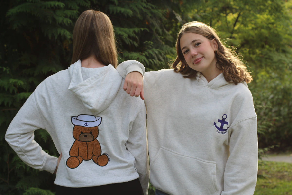 Two people wearing white hoodies with teddy bear and anchor designs outdoors.