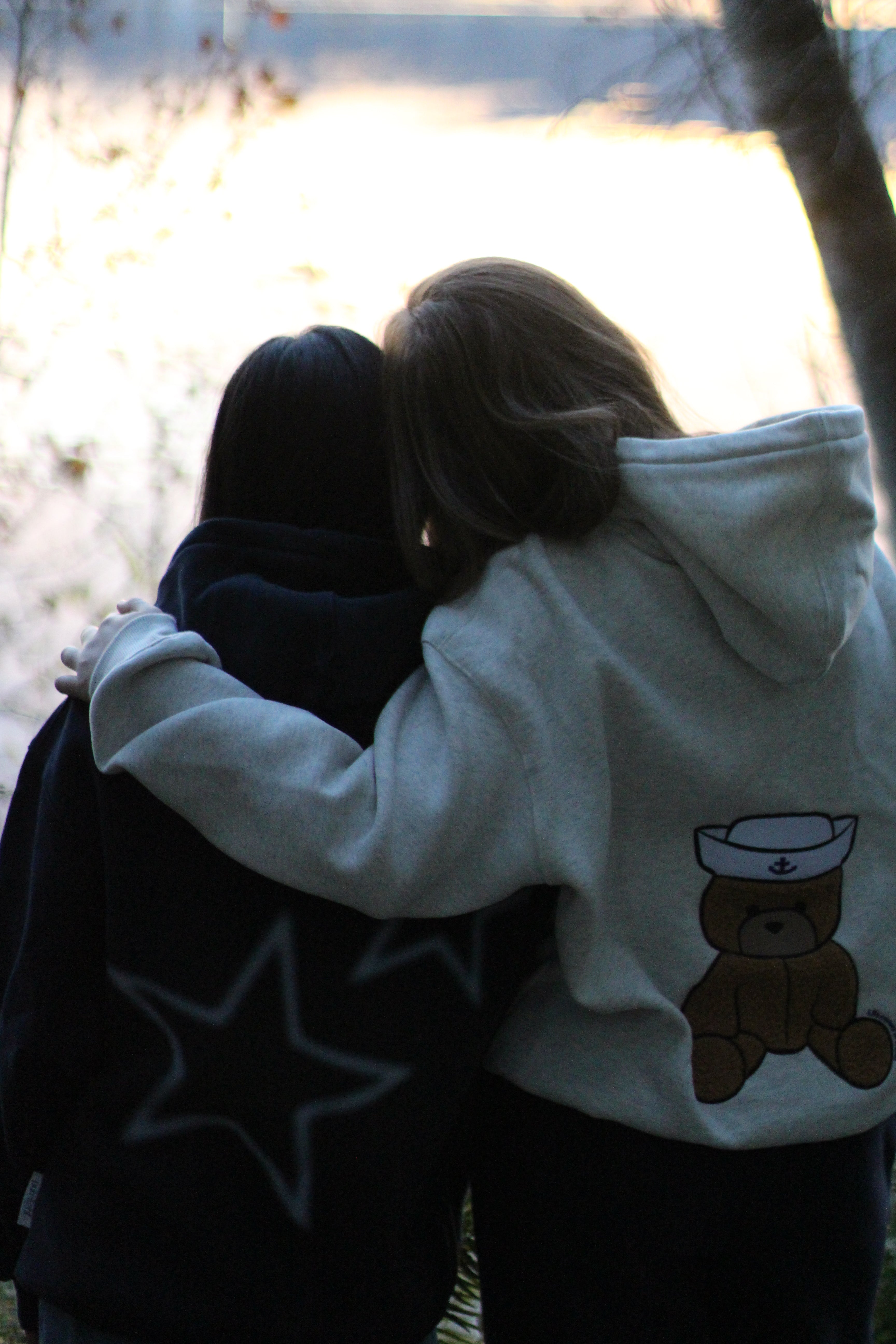 Person wearing a light blue hoodie with a bear design, sitting outdoors.