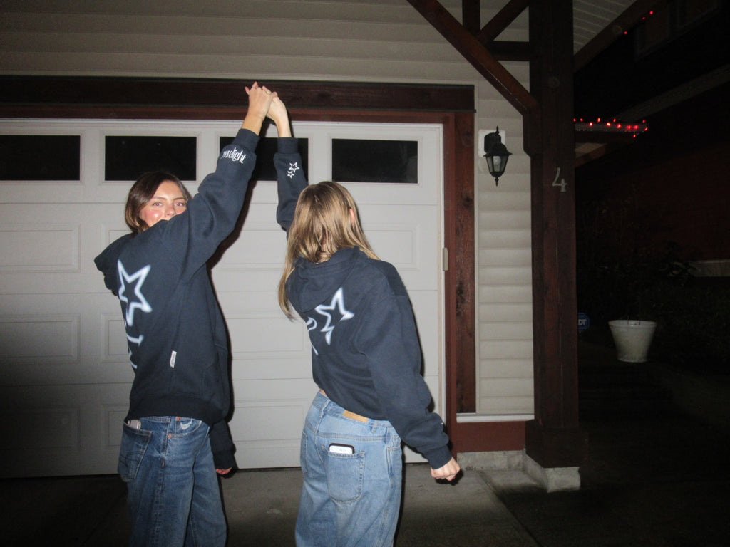 Two people wearing matching sweatshirts with a star design in front of a garage.
