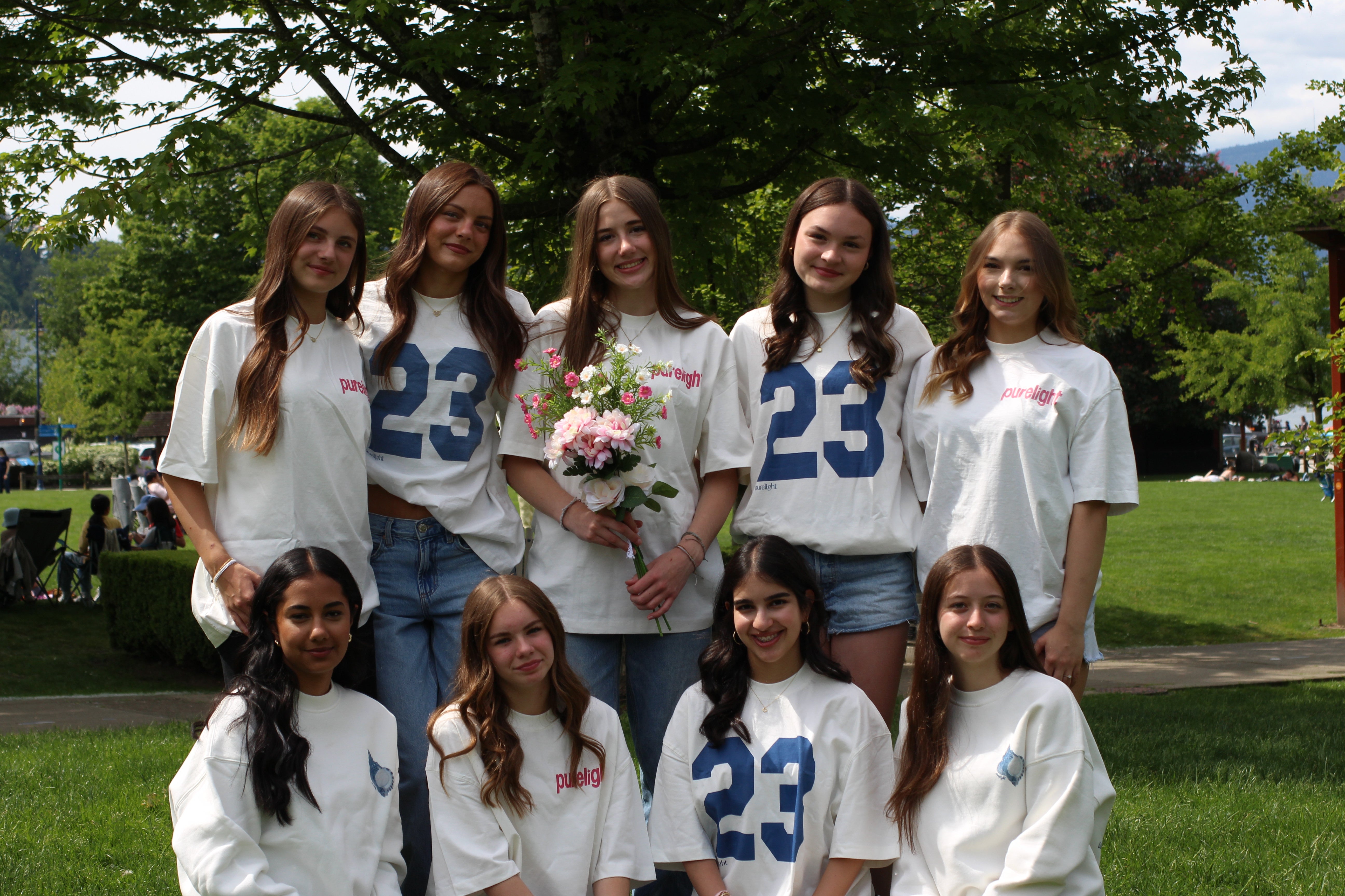 Group of girls wearing matching shirts with the number 23 in a park setting.