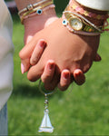 Two people holding hands with visible jewelry against a blurred green background